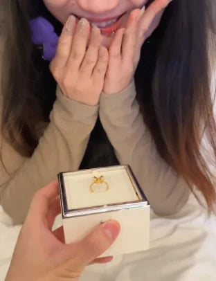 Person holding a ring in a box with another person covering their mouth in excitement.