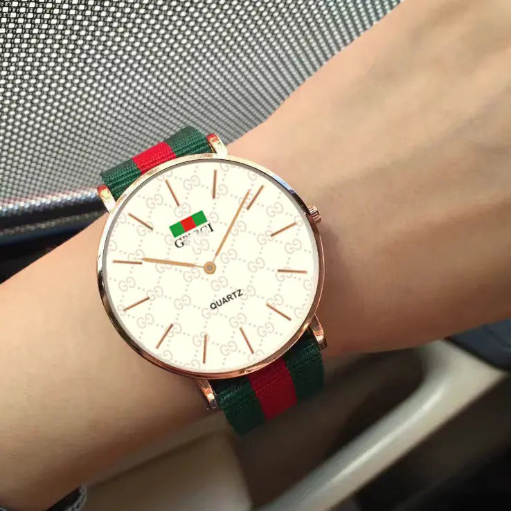 Wrist wearing a watch with a green and red strap on a blurred background