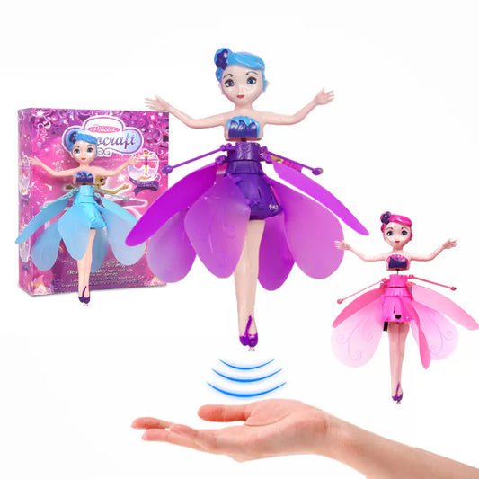 Fairy dolls with purple and pink wings, one being held by a hand, with packaging in the background.
